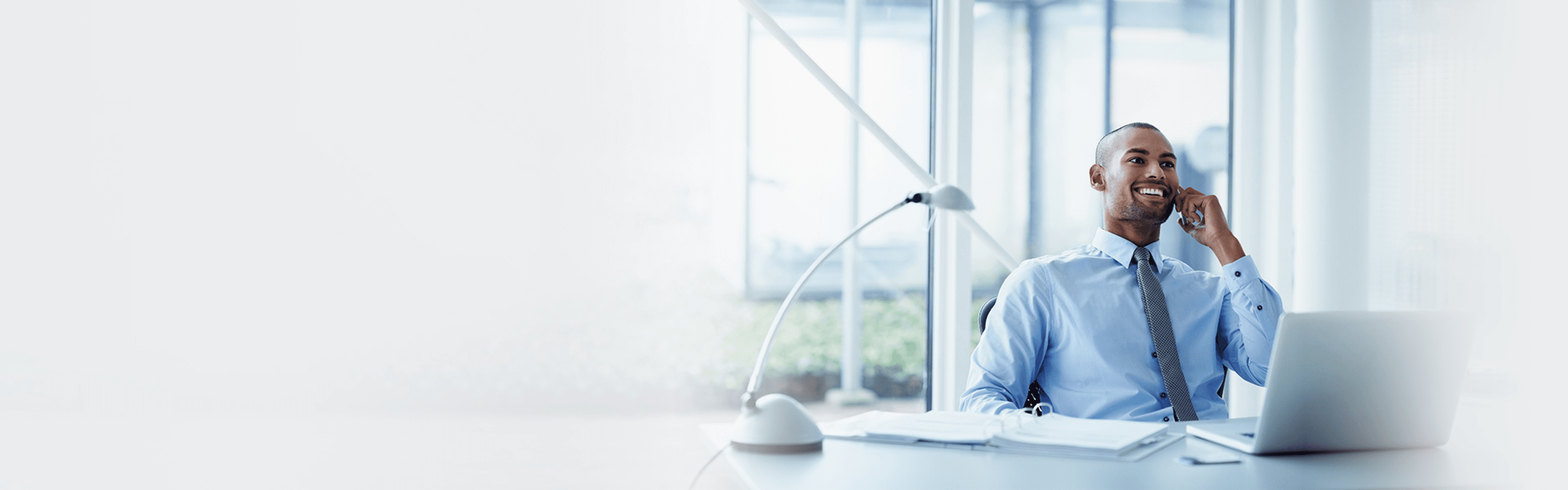 Smiling businessman looking away while using mobile phone at desk in office.