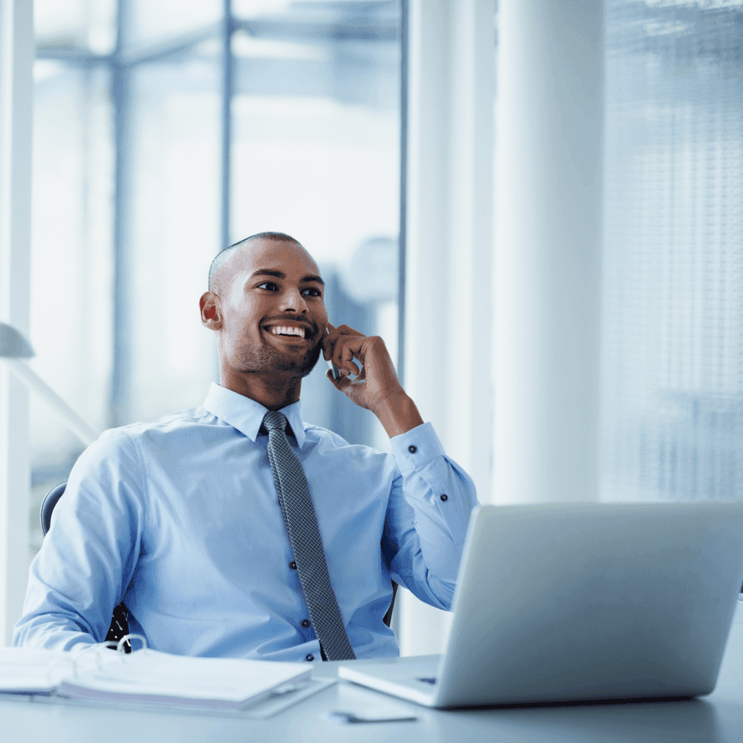 Smiling businessman looking away while using mobile phone at desk in office.