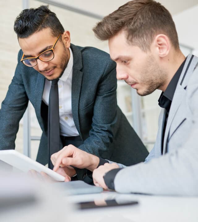 Portrait of young Middle-Eastern entrepreneur using digital tablet while working with colleague at desk in modern office of startup company.